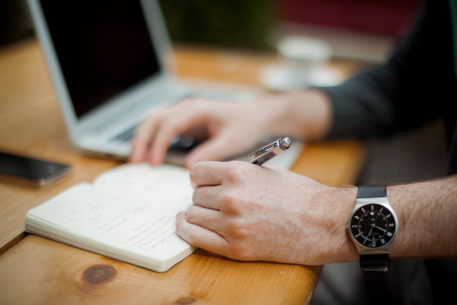 Man writing in a note pad with a laptop